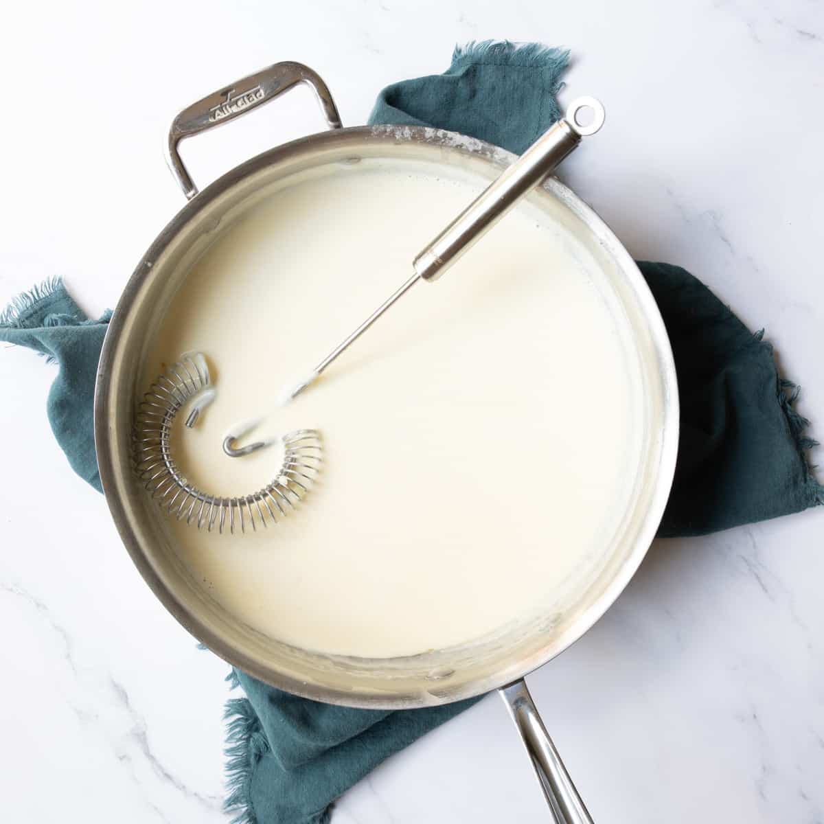 Whisk resting in a pan of thick alfredo sauce for serving with pasta.