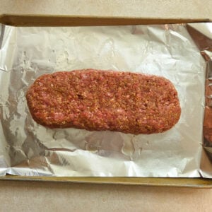 Seasoned ground beef formed into a loaf shape and placed on a foil lined baking sheet.