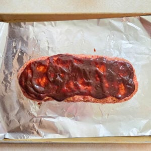 Barbecue glaze covering a raw beef meatloaf loaf ready to bake.
