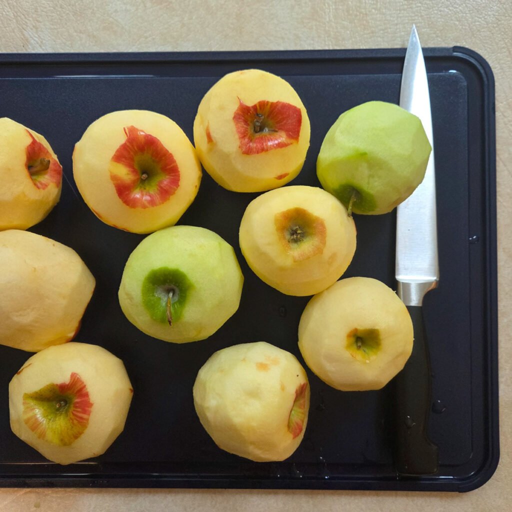 Peeled apples laying on a cutting board next to a sharp knife.