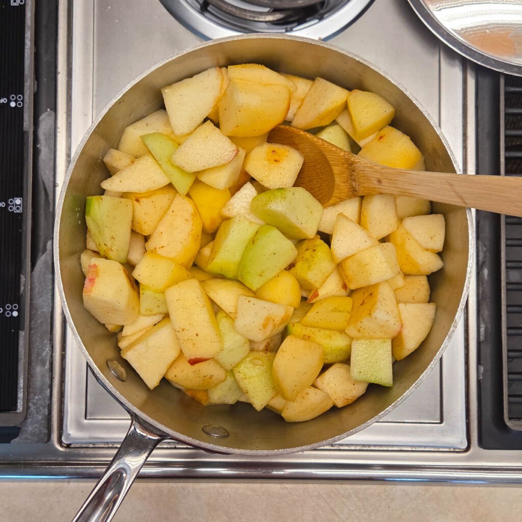 Wooden spoon resting in a mixture of softened apples cooking in a skillet.