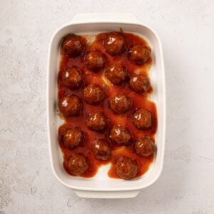 Meatballs in a rectangular baking dish topped with sweet and sour glaze.