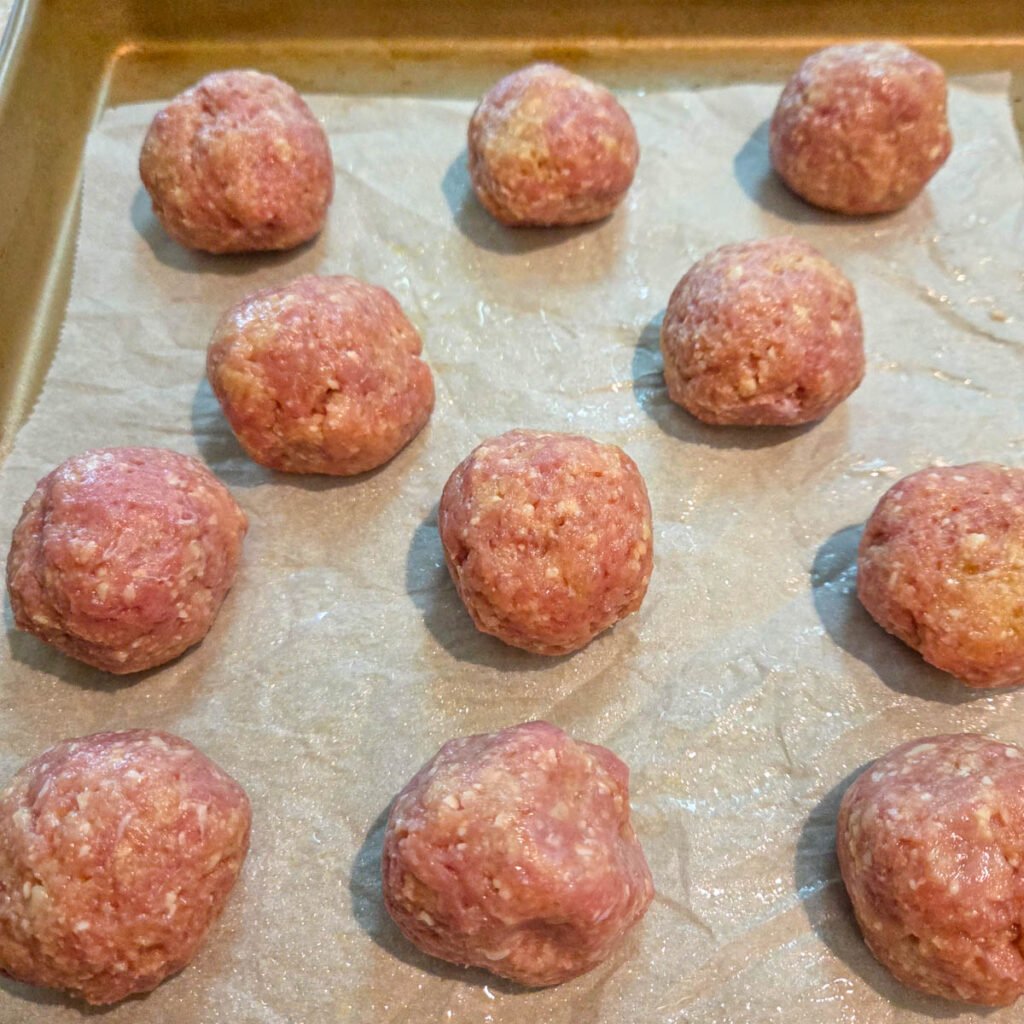 Raw ground turkey meatballs resting on parchment paper over a baking sheet.