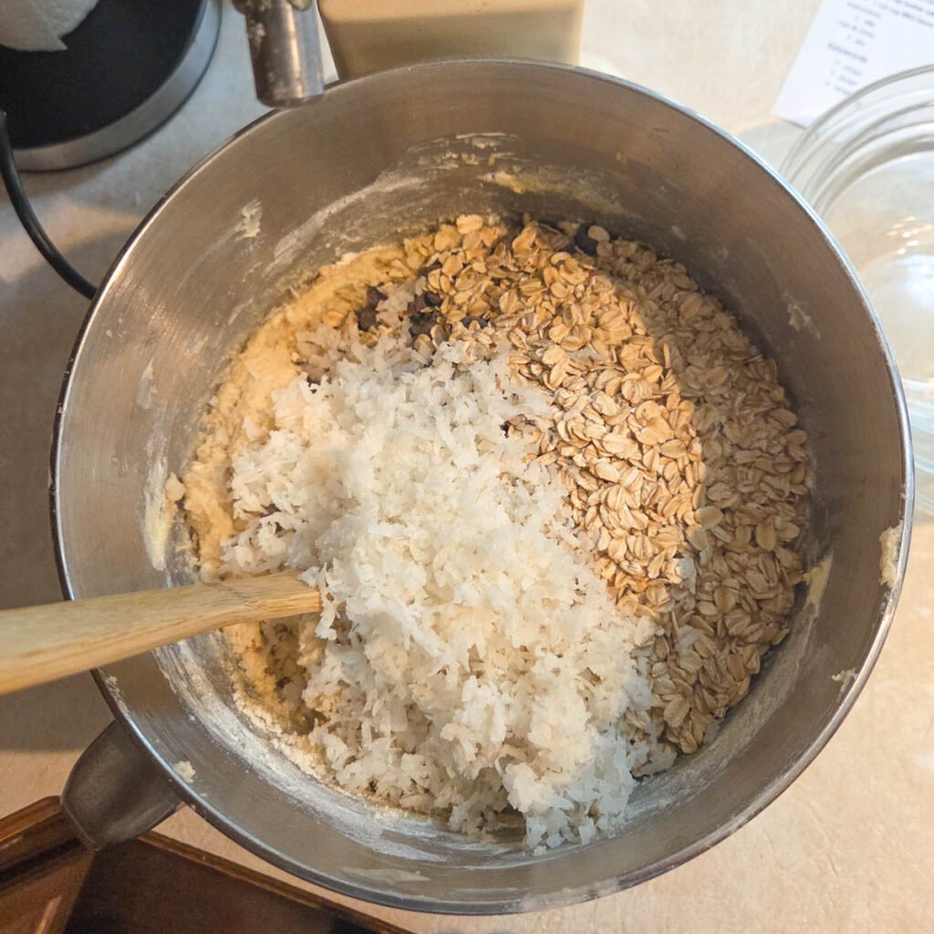 Coconut, oatmeal added to the batter of the dough in a mixing bowl.