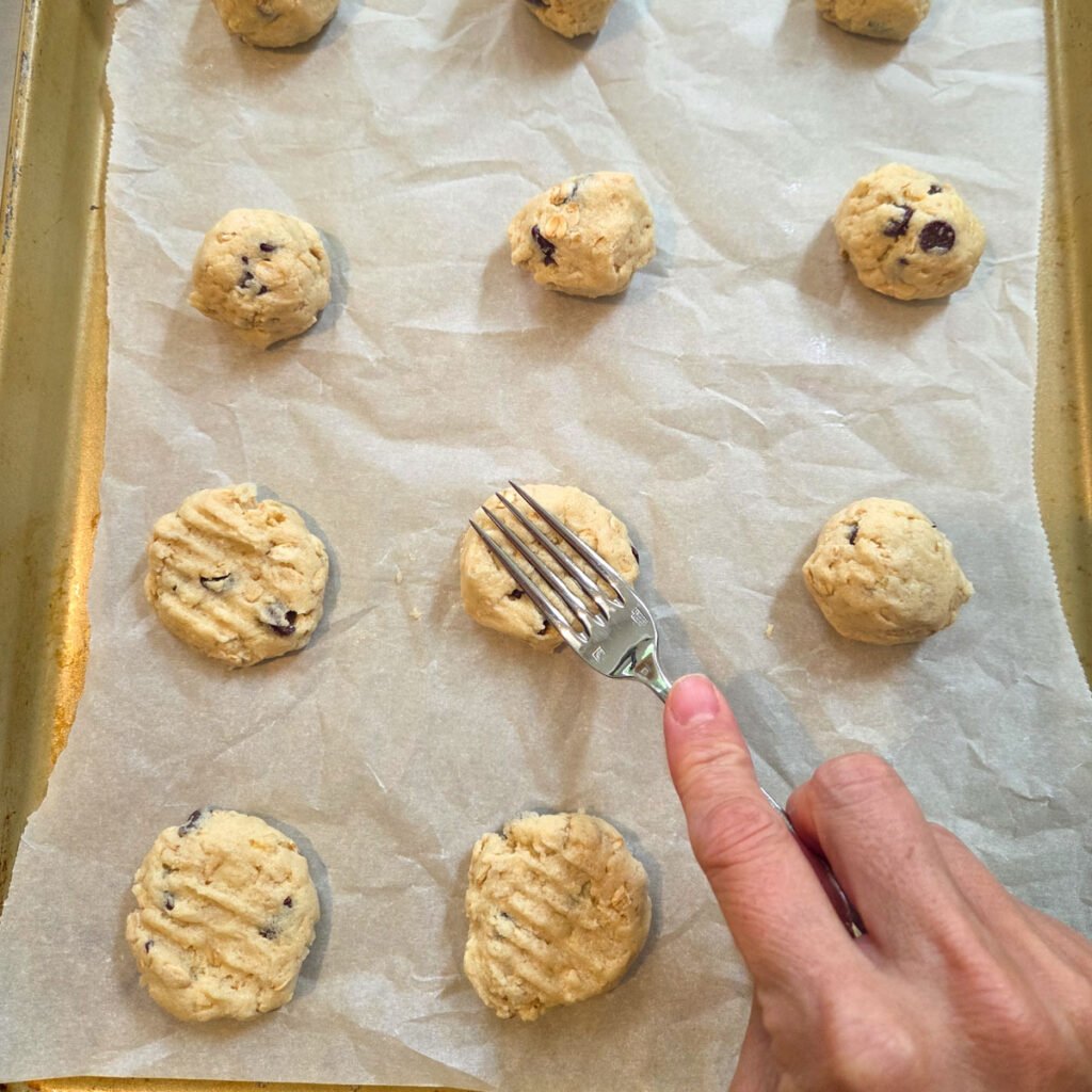 Fork flattening 100 Good Cookie dough balls onto parchment paper before baking.