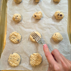 Fork flattening 100 Good Cookie dough balls onto parchment paper before baking.