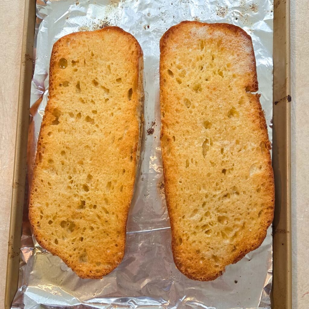Toasted halves of French bread laying on a baking sheet