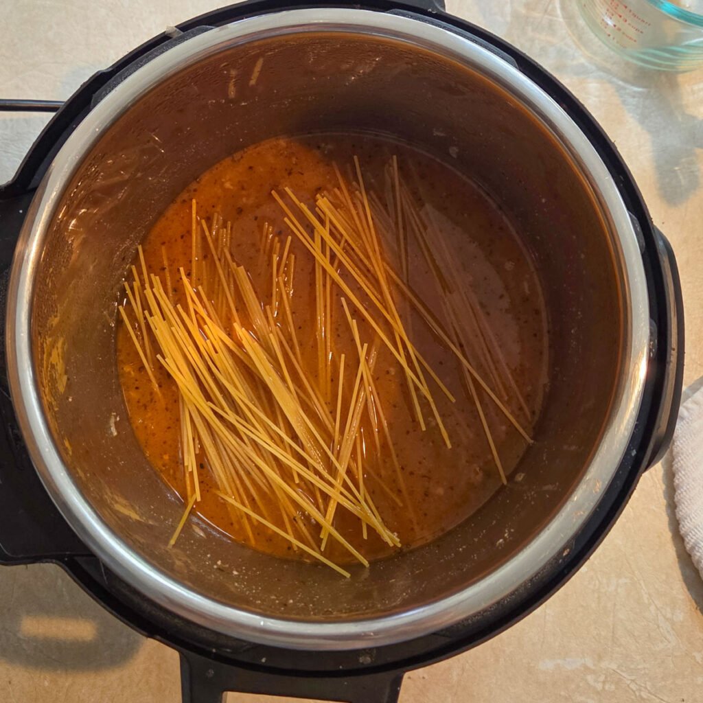Chicken broth added to the instant pot with spaghetti noodles added to the top of the mixture.