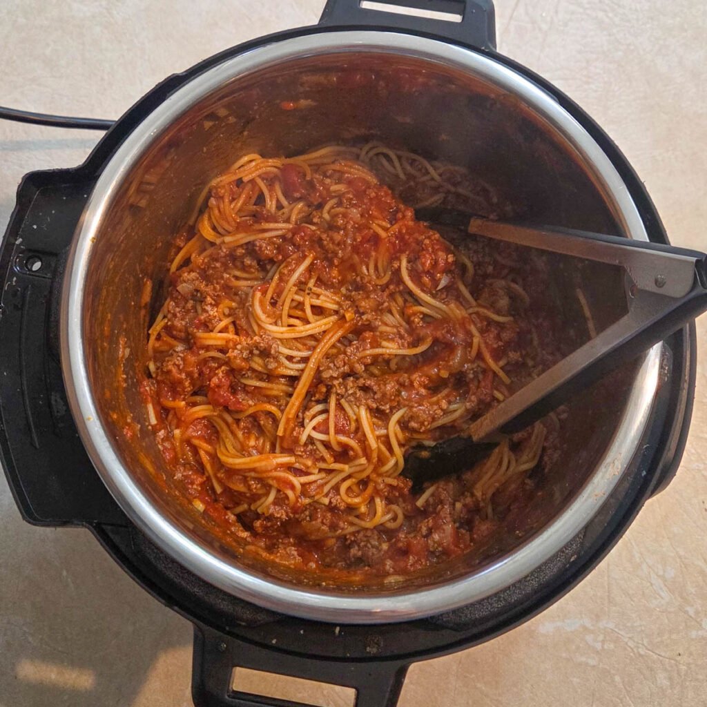 Meat sauce ready to serve inside the instant pot with tongs resting in the mixture.
