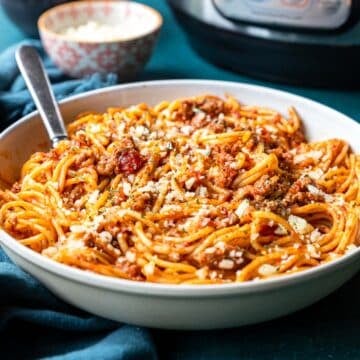 A bowl of spaghetti with meat sauce and the instant pot sitting in the back
