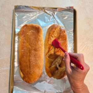Silicone brush adding garlic butter to the bottoms of an Italian loaf.