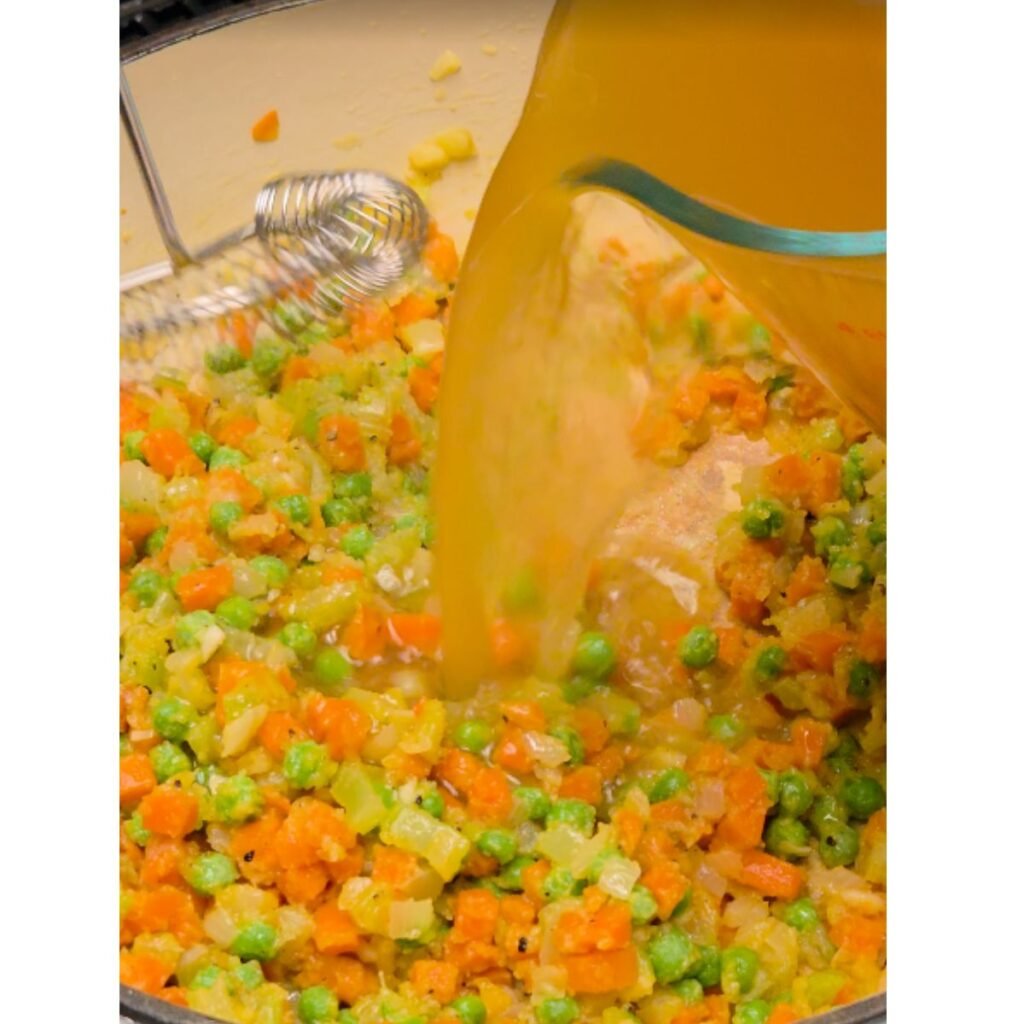 chicken broth being stirred into veggies with a flour roux
