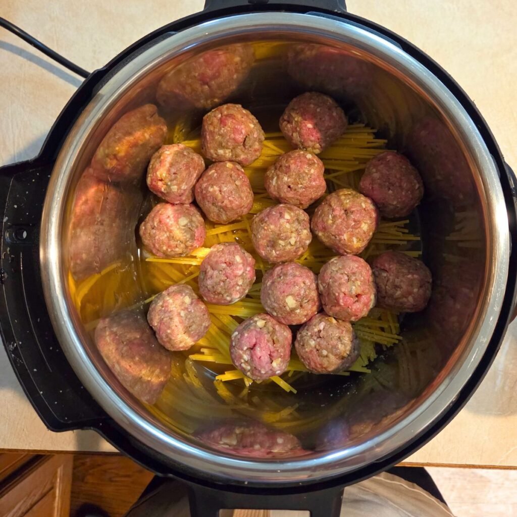 Raw meatballs added to the top of the uncooked pasta in the instant pot.