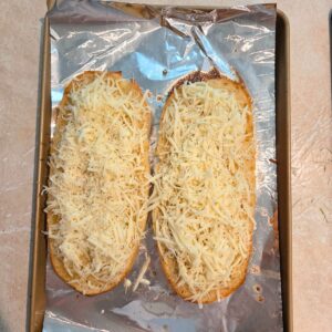 Shredded cheese added to the two halves of a garlic butter topped loaf of Italian bread.