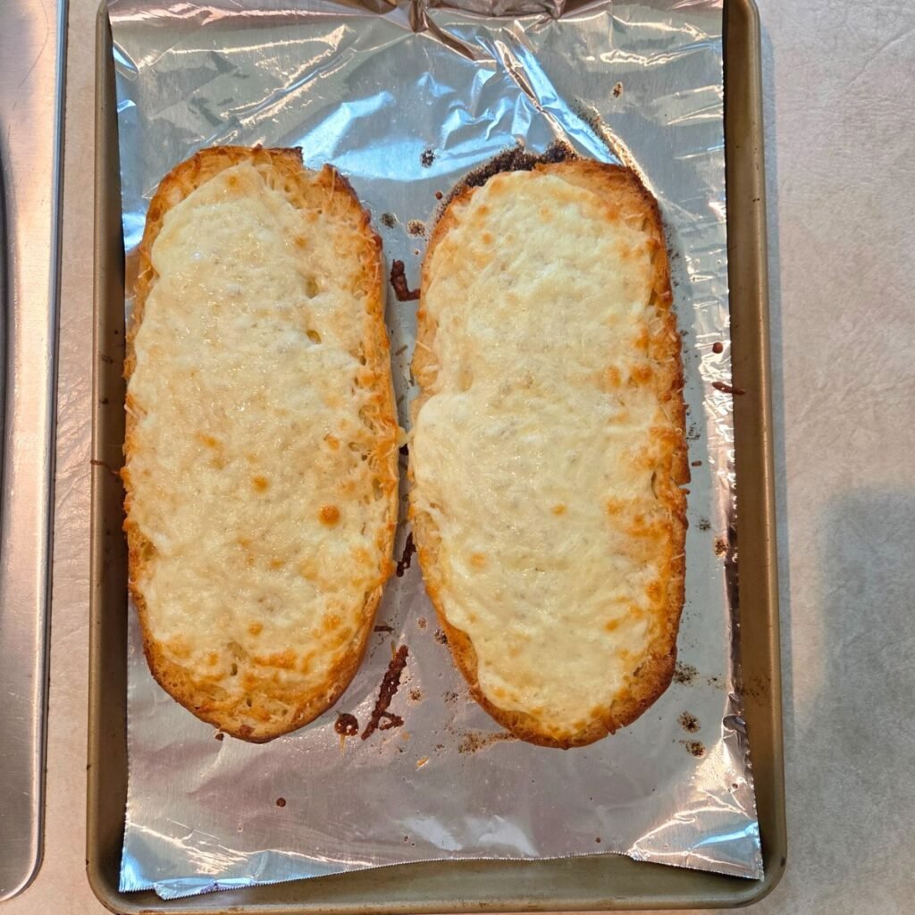 Golden brown cheesy bread with garlic on an aluminum foil topped baking sheet.