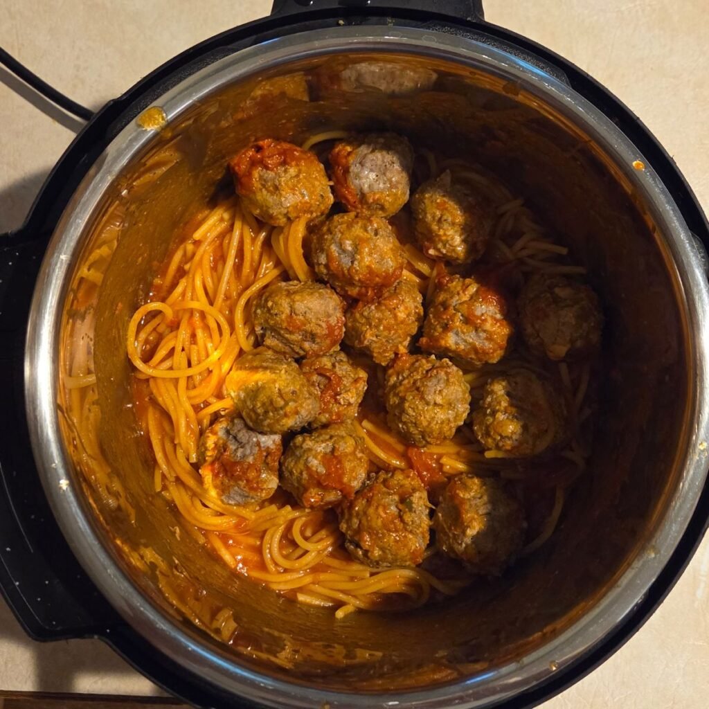 Meatballs resting in the instant pot on top of the spaghetti and pasta.