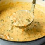 Ladleful of broccoli cheddar soup coming out of a Dutch oven, ready to serve.