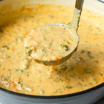 Ladleful of broccoli cheddar soup coming out of a Dutch oven, ready to serve.