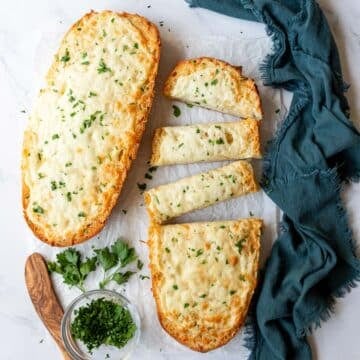 Parsley topped garlic cheesy bread with half of the loaf sliced into individual pieces to serve.