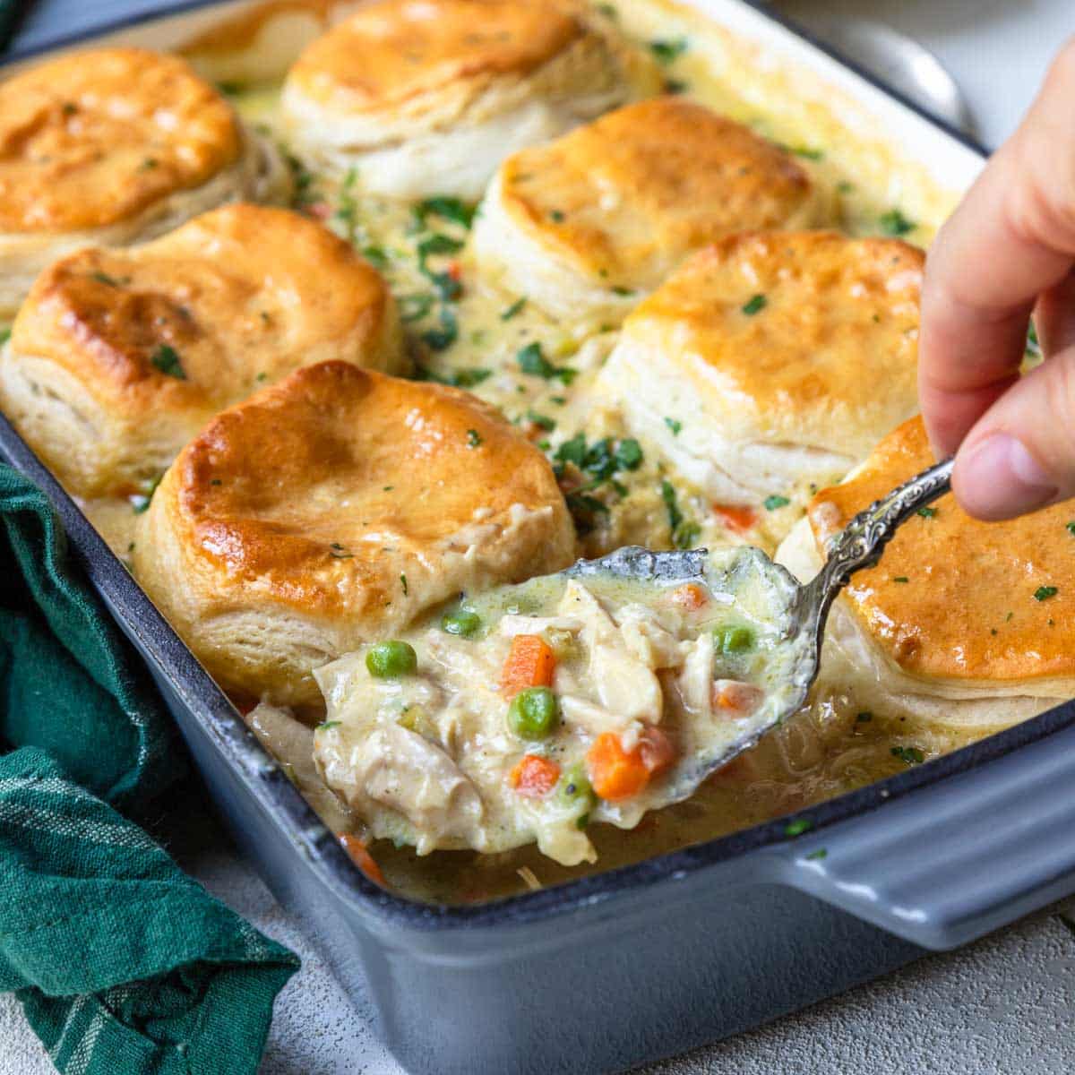 spooning the chicken filling out of a casserole pan of chicken and biscuits 