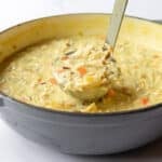 Soup ladle full of creamy chicken wild rice soup pulling up out of the Dutch oven pot.