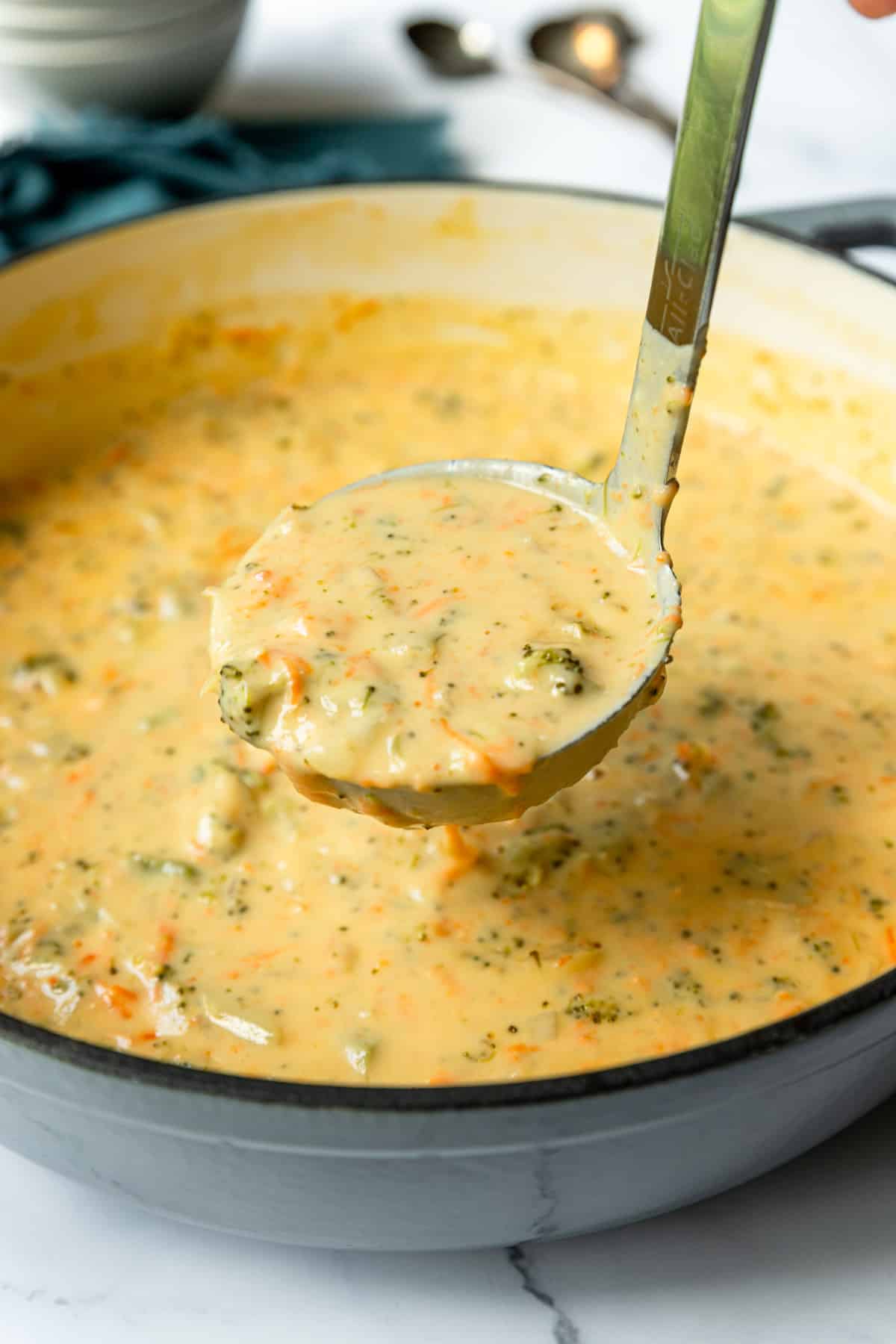 Ladle of broccoli cheddar soup pulling out of a Dutch oven pan.