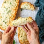 Hand holding up a golden brown baked piece of cheesy garlic bread.