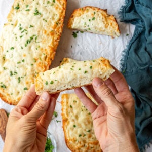 Hand holding up a golden brown baked piece of cheesy garlic bread.