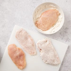 Thin cut chicken breasts dredged in flour and laid out on a cutting board before cooking.