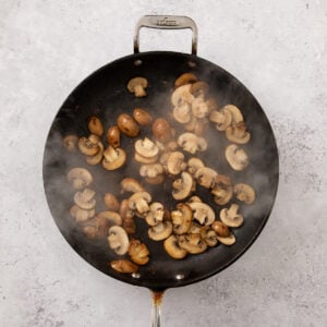 Sliced baby bella mushrooms sauteeing in a skillet.