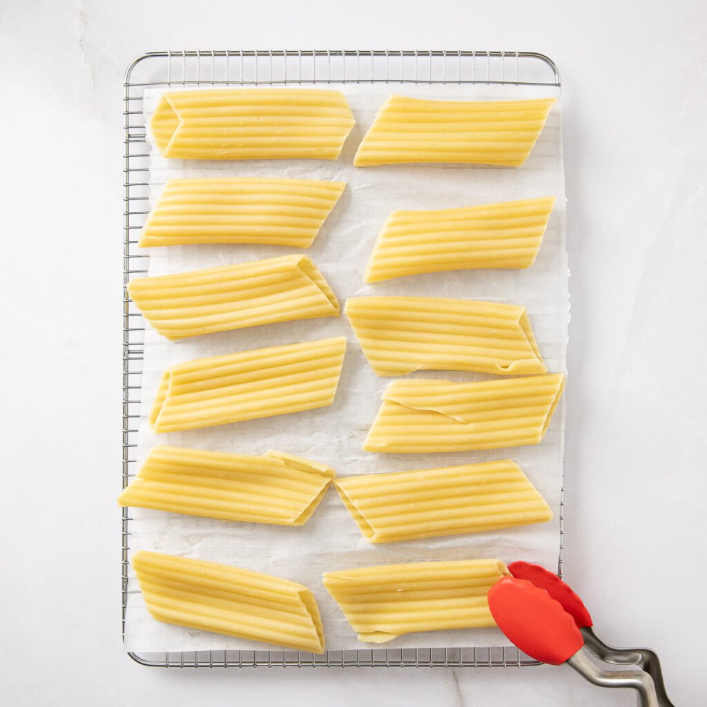 Cooked manicotti shells cooling on a parchment paper coated cooling rack.