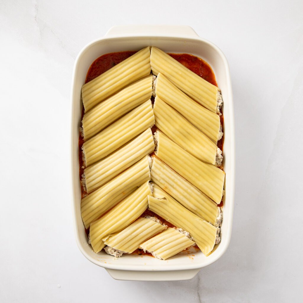 Stuffed manicotti shells added to a baking dish with marinara sauce on the bottom.