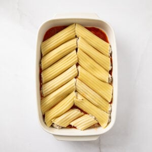 Stuffed manicotti shells added to a baking dish with marinara sauce on the bottom.