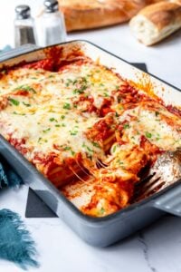 A few slices of stuffed beef manicotti served from a baking dish with melted cheese spilling out into the serving fork resting there.