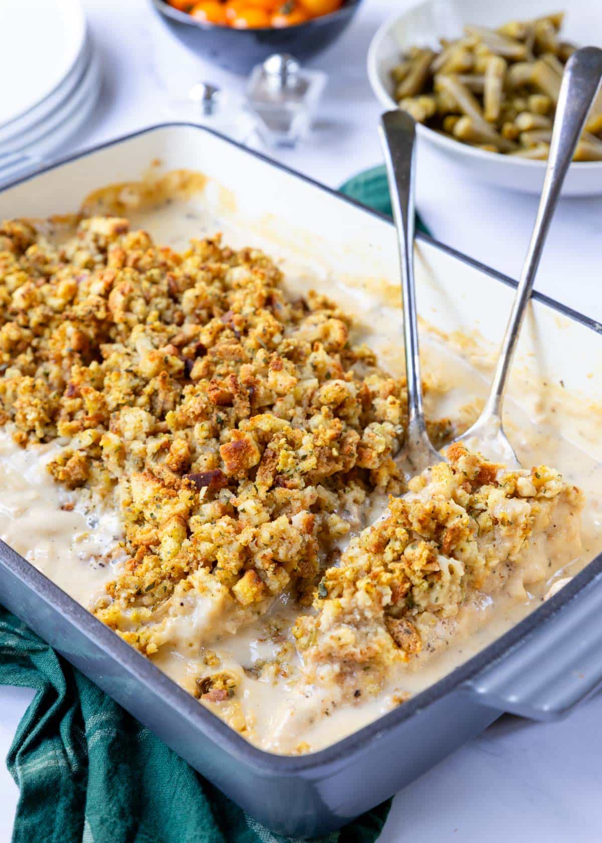 A pan of chicken and stuffing with green beans and tomatoes in the background 