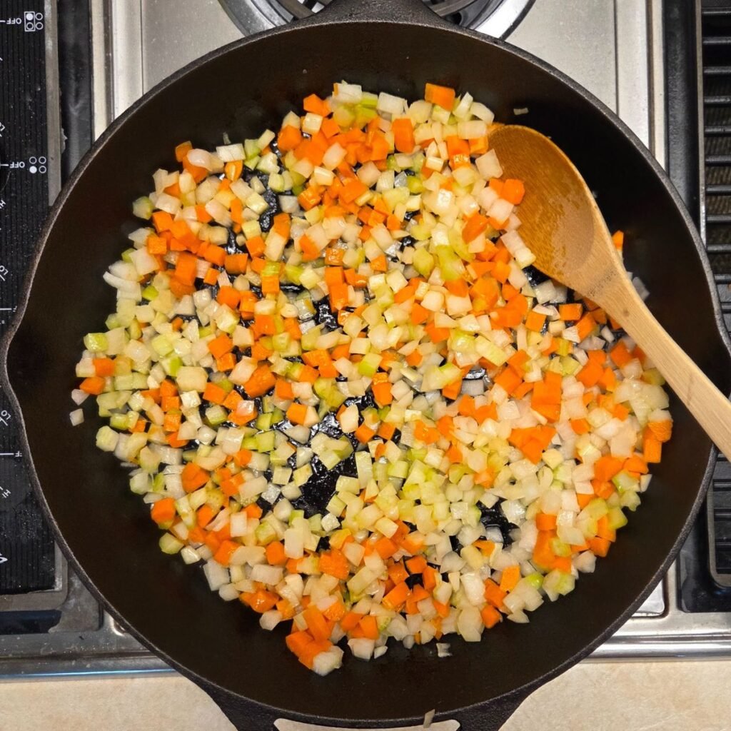 Chopped onions, carrots sauteeing in a skillet.