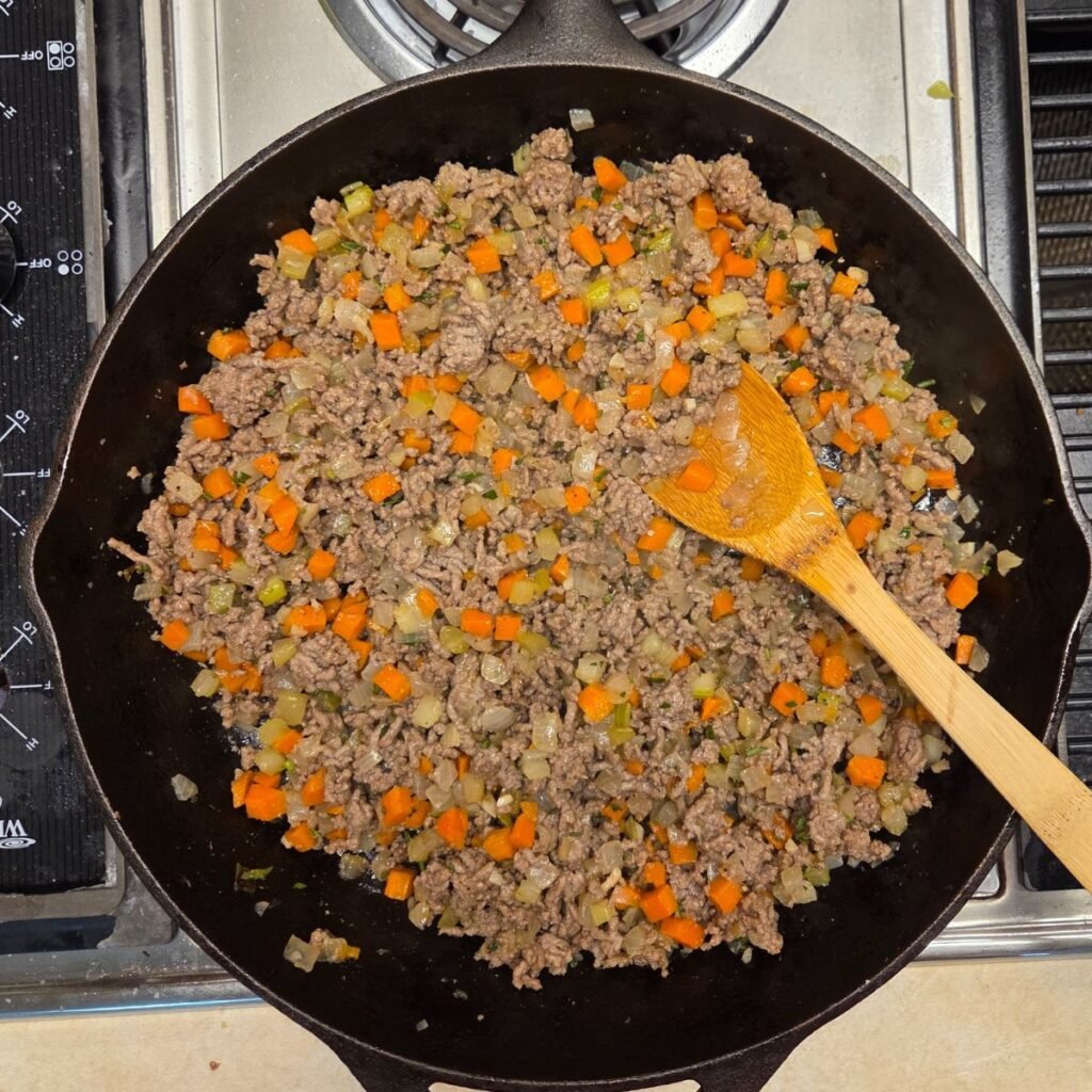 Woode spoon resting in onion, carrots and ground beef mixture.