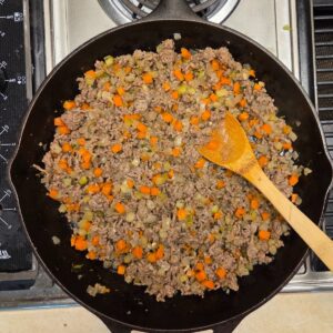 Woode spoon resting in onion, carrots and ground beef mixture.