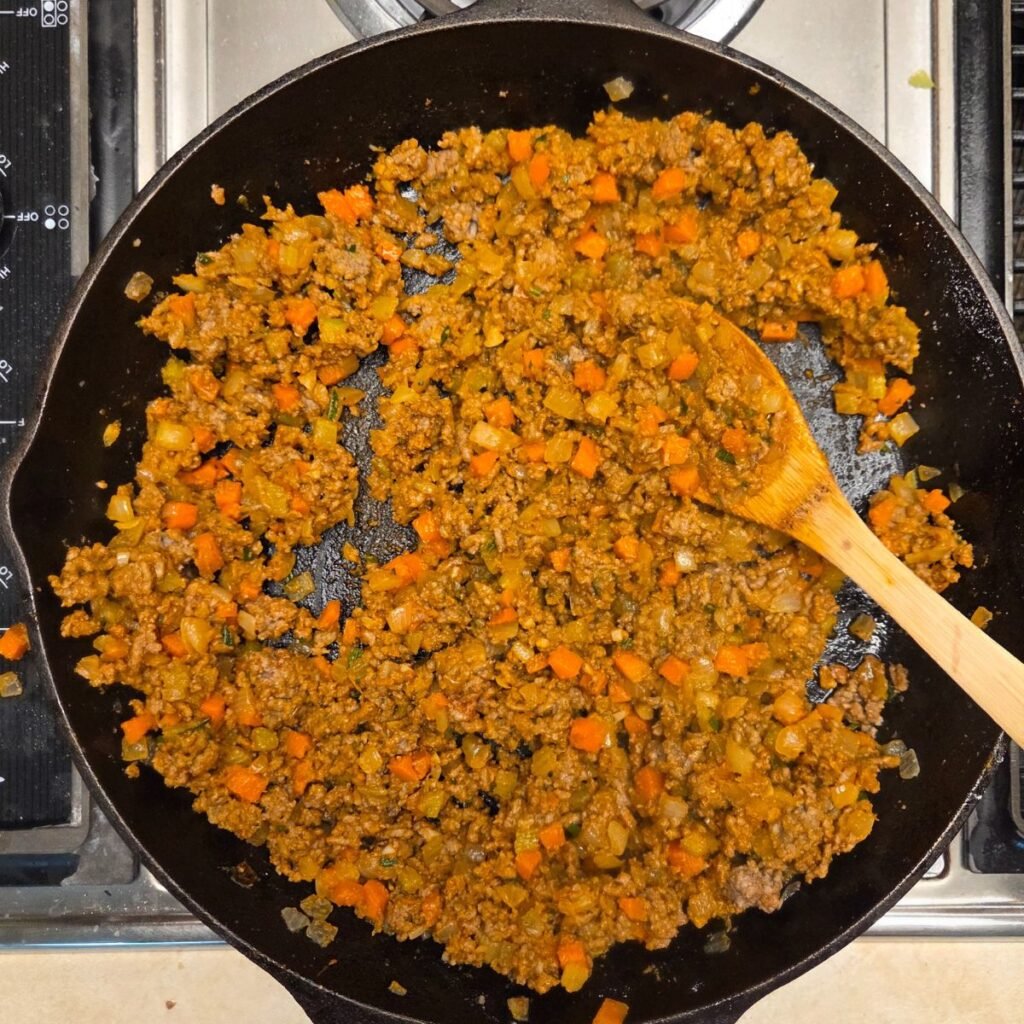 Browned ground beef and carrots with chopped onions in a skillet.