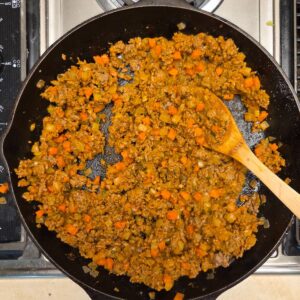 Browned ground beef and carrots with chopped onions in a skillet.