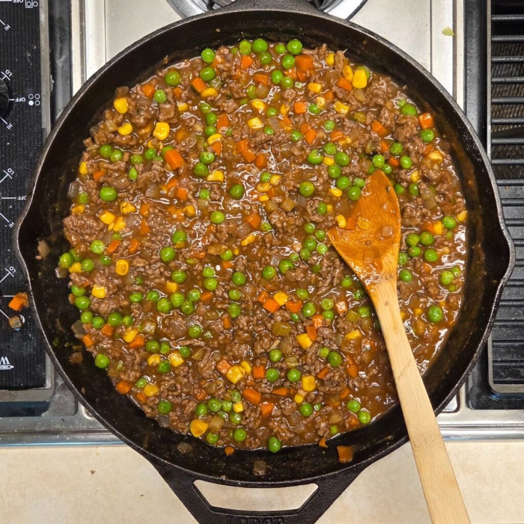 Wooden spoon resting a skillet with mixed veggies and ground beef mixture.