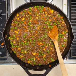 Wooden spoon resting a skillet with mixed veggies and ground beef mixture.