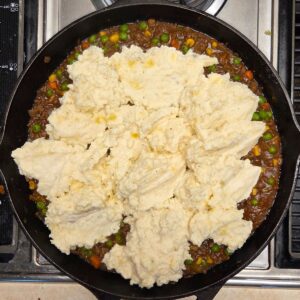 Dollops of mashed potatoes added to a skillet with beef and veggie mixture.