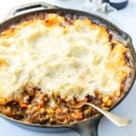 Spoon resting in a veggie and beef gravy mixture topped with a thick measure of mashed potatoes.