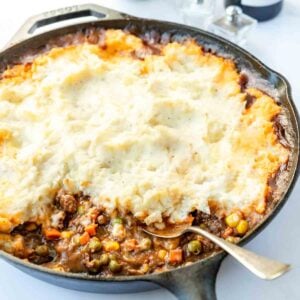 Spoon resting in a veggie and beef gravy mixture topped with a thick measure of mashed potatoes.
