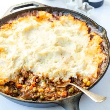 Spoon resting in a veggie and beef gravy mixture topped with a thick measure of mashed potatoes.