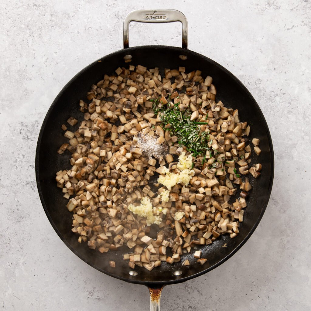 Seasonings topping pancetta and diced mushrooms with pancetta in a skillet.