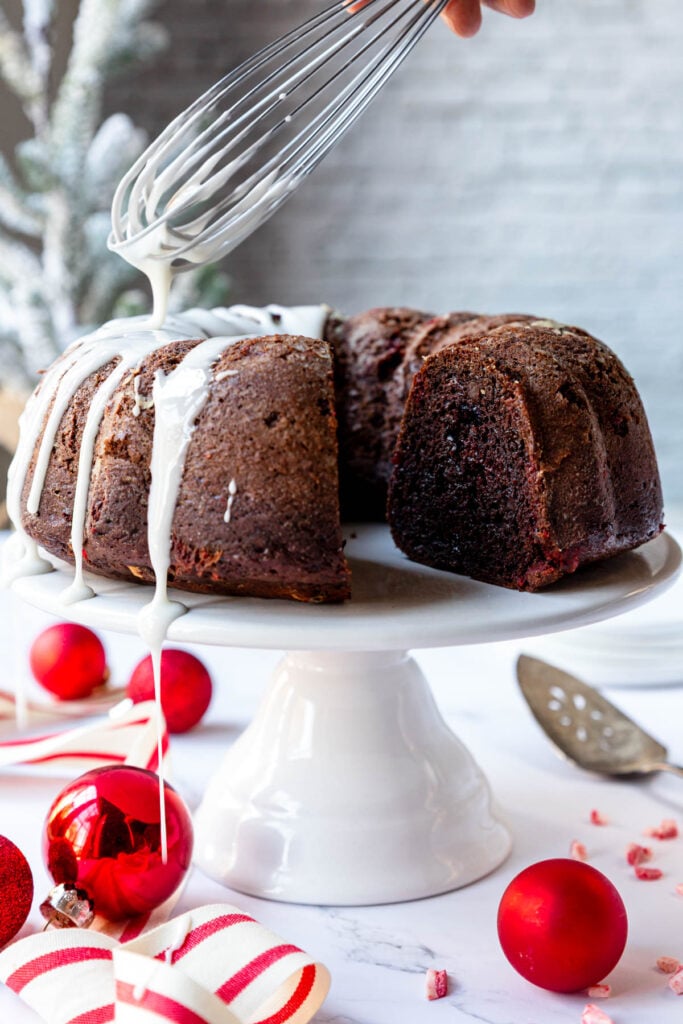 Whisk drizzling a glaze over a peppermint chocolate bundt cake on a cake stand.