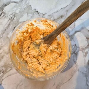 Chicken chunks being combined with Franks red sauce in a glass mixing bowl.