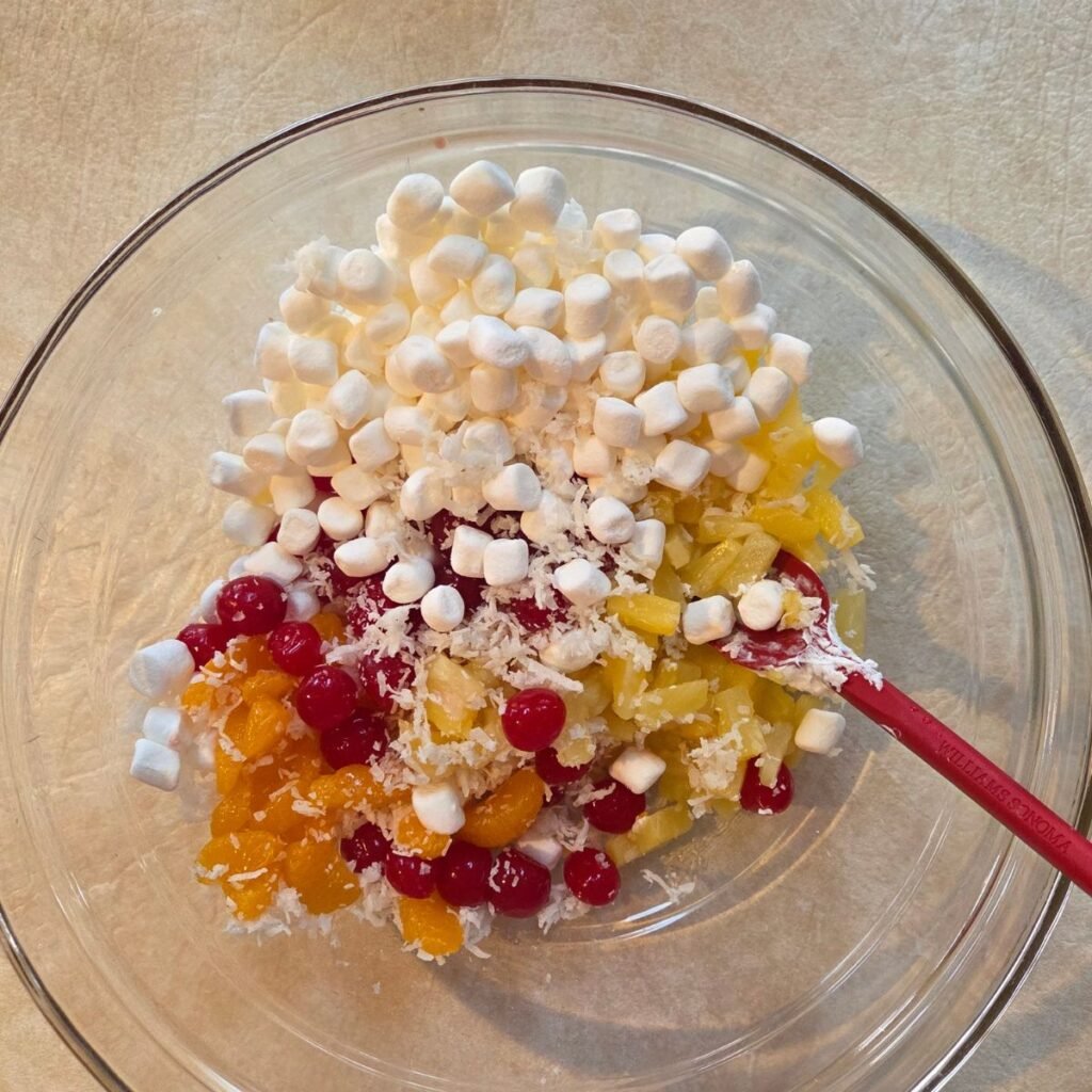 Ambrosia salad ingredients added to a glass mixing bowl.